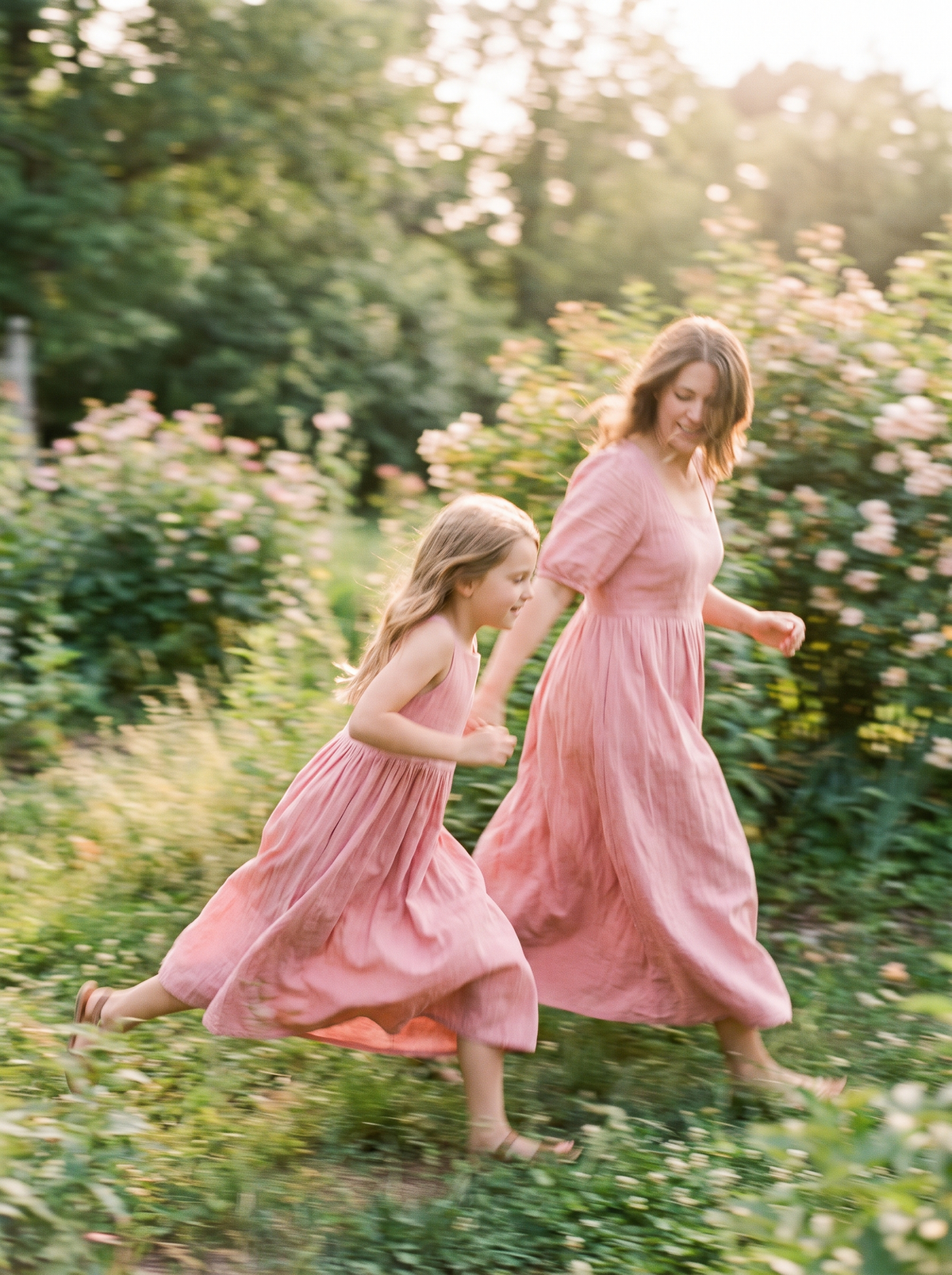 A girl and a woman in matching dresses running through a garden